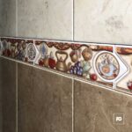 Decorative ceramic tile border with fruit, teapots, and kitchen motifs along a tiled wall.