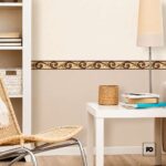 Cozy reading nook with a white desk, stack of books, woven basket, and a wicker chair against a beige wall with decorative border.