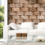 Modern living room with a white sofa, glass coffee table, two small wooden boxes, and a beige stone accent wall.