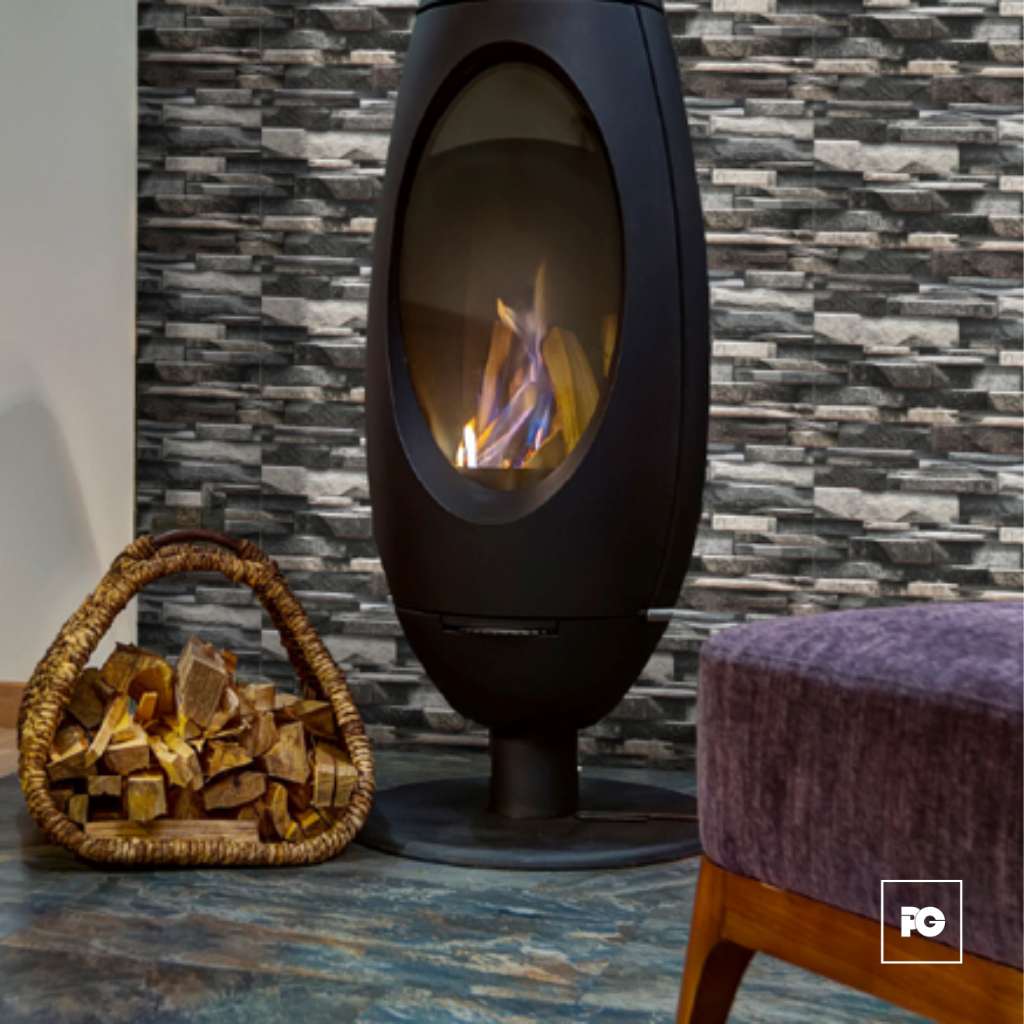Contemporary freestanding fireplace with a glass front burning logs, next to a basket of firewood and a purple upholstered stool in a living room.