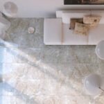 Xrddaft5nfpyno368j8524596904441476622t23111000 | Plomería García Top-down view of a modern living room with a white sectional sofa and patterned throw pillows on a marble-tiled floor. A geometric white floor lamp and round side table are visible.