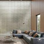 Modern living room with a blue-gray sectional, neutral pillows, glass coffee table, and a glass-block wall.