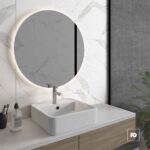 Round backlit mirror above a white rectangular sink on a marble backsplash and wooden vanity in a modern bathroom.